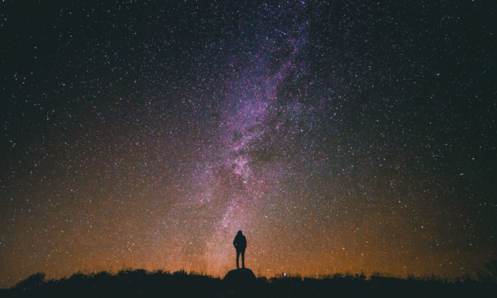 Person standing on a rock looking up at the stars at night