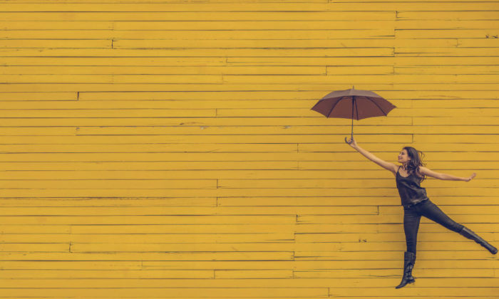 Woman with an umbrella with a yellow wall behind her as she jumps towards mastering lifecycle marketing emails