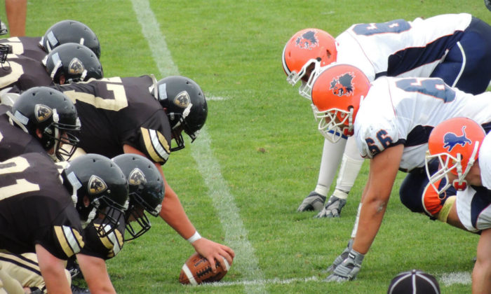 American football match with a white team jersey and a black team jersey. The black jersey quarterback has the football.