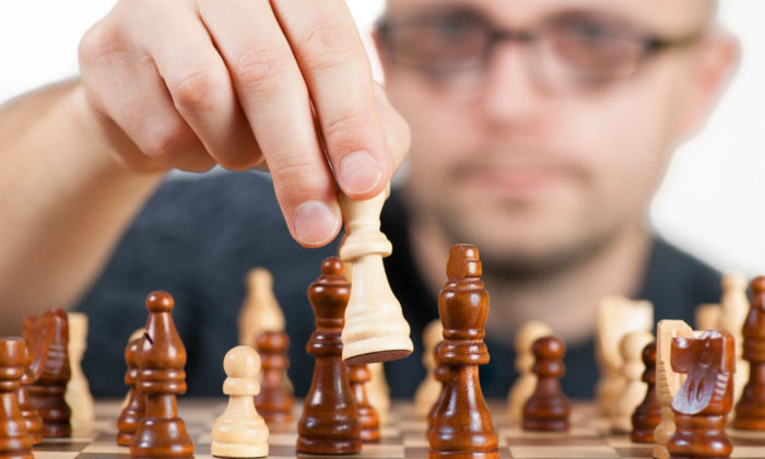 Man playing chess and moving a piece strategically. His face is out of focus.