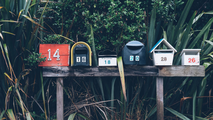 Six mailboxes in a row with lush green plants behind